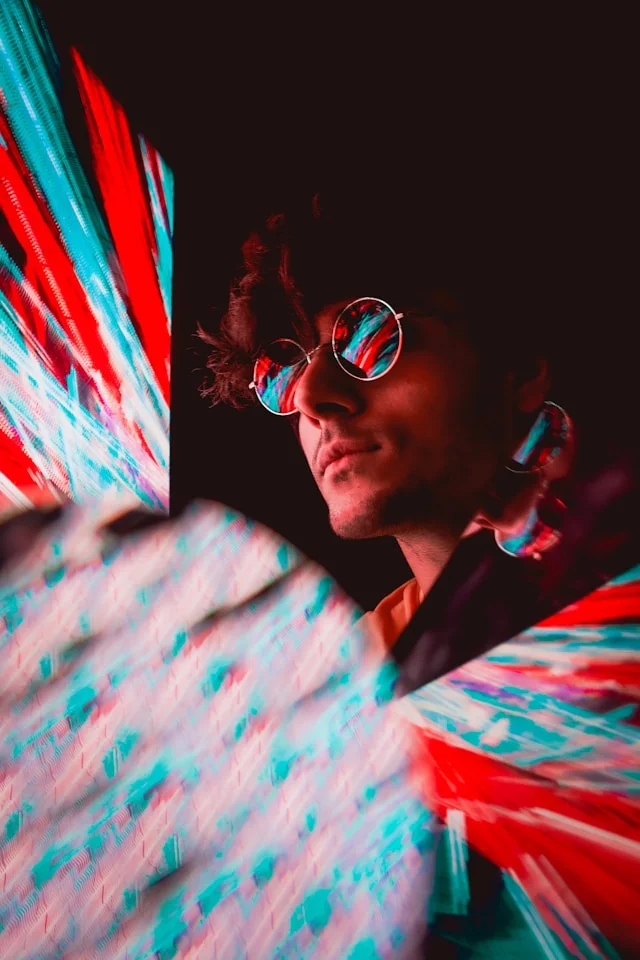 A man in round glasses looking ahead, streaks of red and blue light crossing the frame