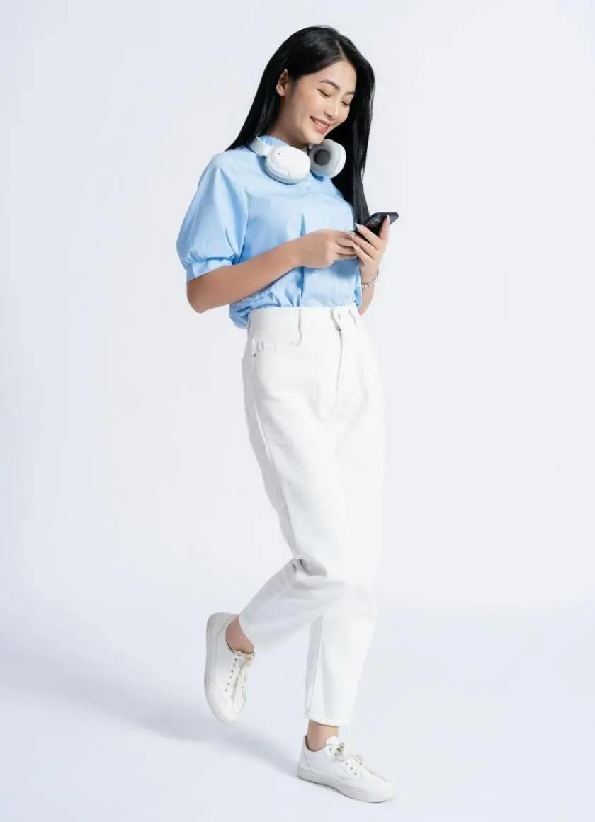 A woman with headphones around her neck smiling at her phone as she walks